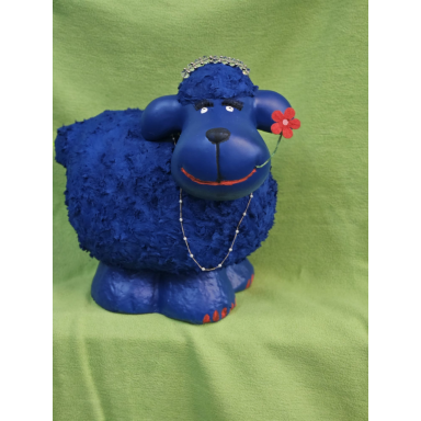 Das blaue Blumenschaf Kräftig blaue, rundliche Schaffigur mit roter Blume am Ohr, kleinen roten Akzenten und einer Halskette vor grünem Hintergrund.