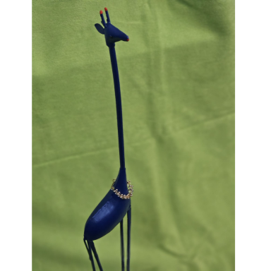 Die blaue Giraffe Schlanke dunkelblaue Giraffenskulptur mit außergewöhnlich langem Hals, dünnen Beinen und einer goldfarbenen Halsverzierung vor grünem Hinter