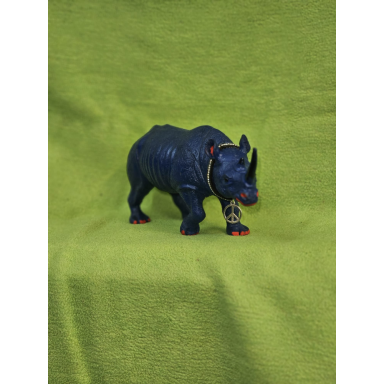 Das kleine blaue Nashorn Kleine dunkelblaue Nashornfigur mit zwei Hörnern, roten Akzenten und einer goldfarbenen Friedenszeichen-Kette vor grünem Hintergrund.