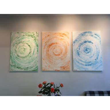 Drei Farben, eine Form Drei abstrakte Gemälde mit grünen, orangefarbenen und blauen Kreisstrukturen hängen nebeneinander an einer grauen Wand.
